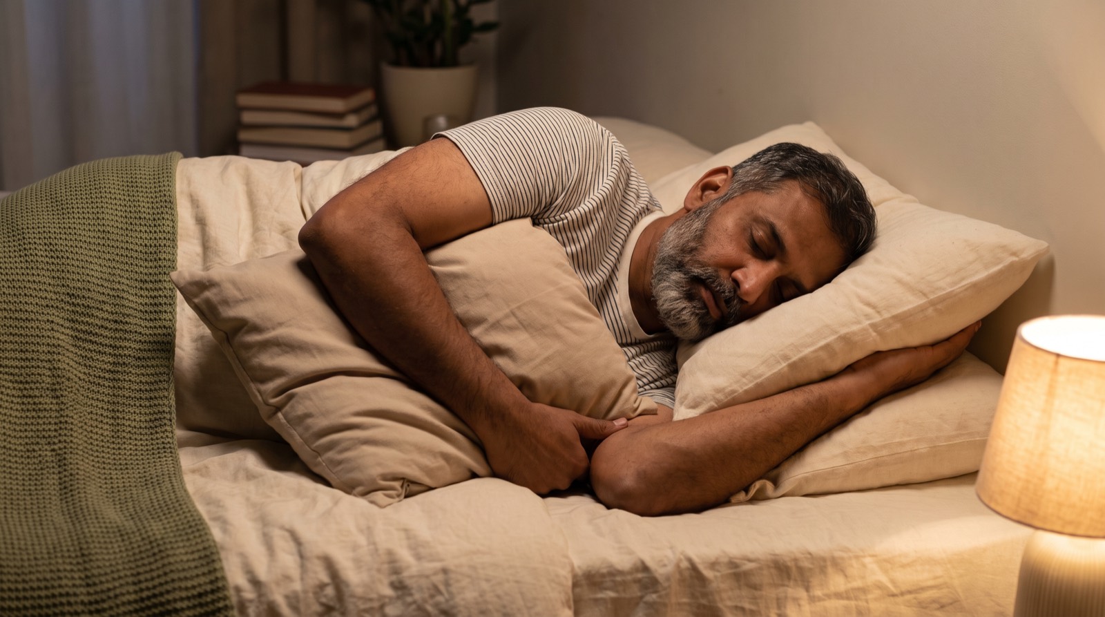 A man sleeping on his side with a pillow hugged under his upper arm so the top shoulder is supported